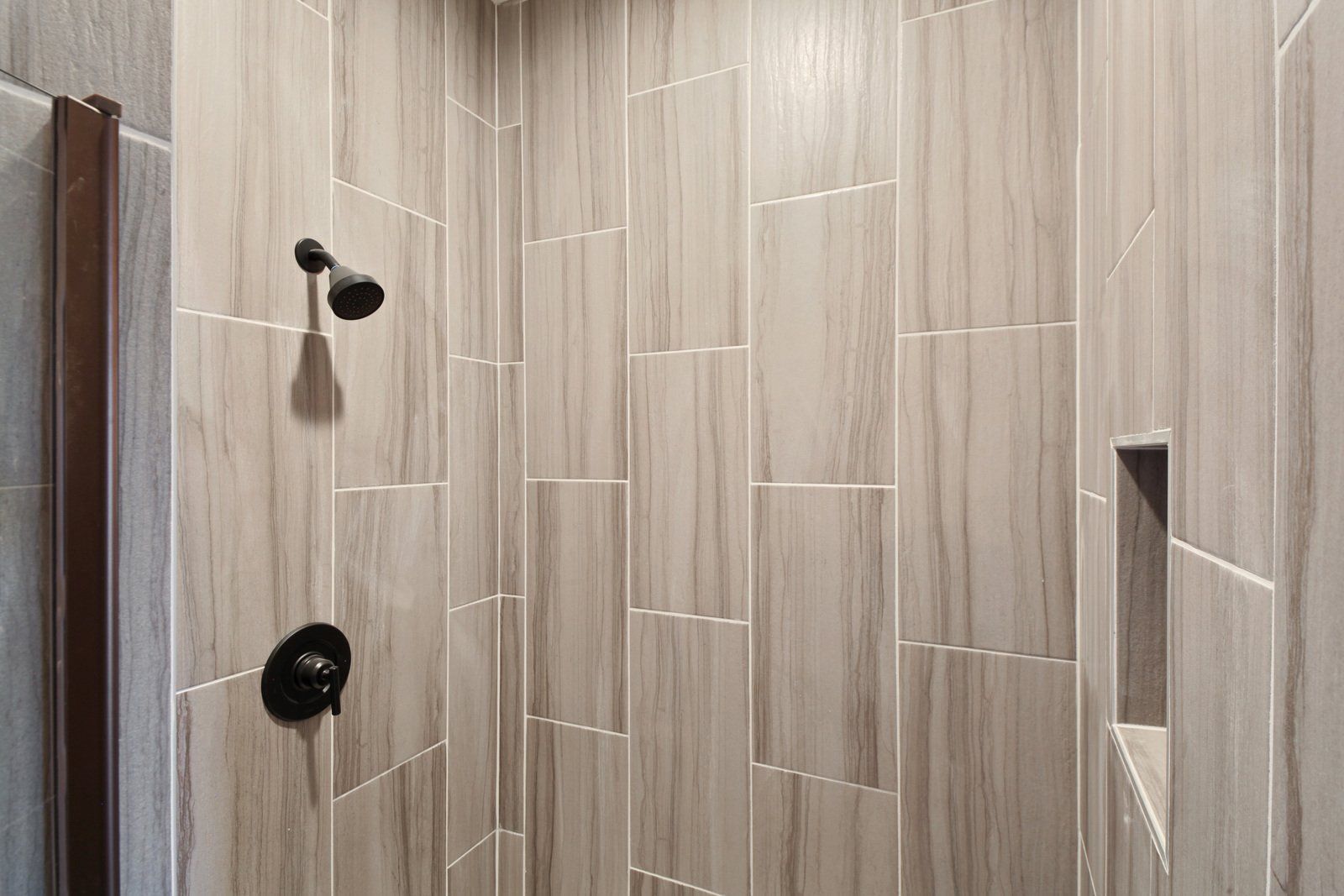 A bathroom with a walk in shower with tile walls and a black shower head.