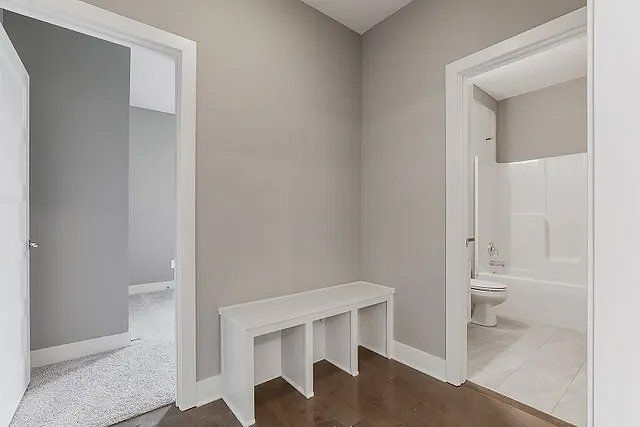 A hallway in a house with a bench and a bathroom.