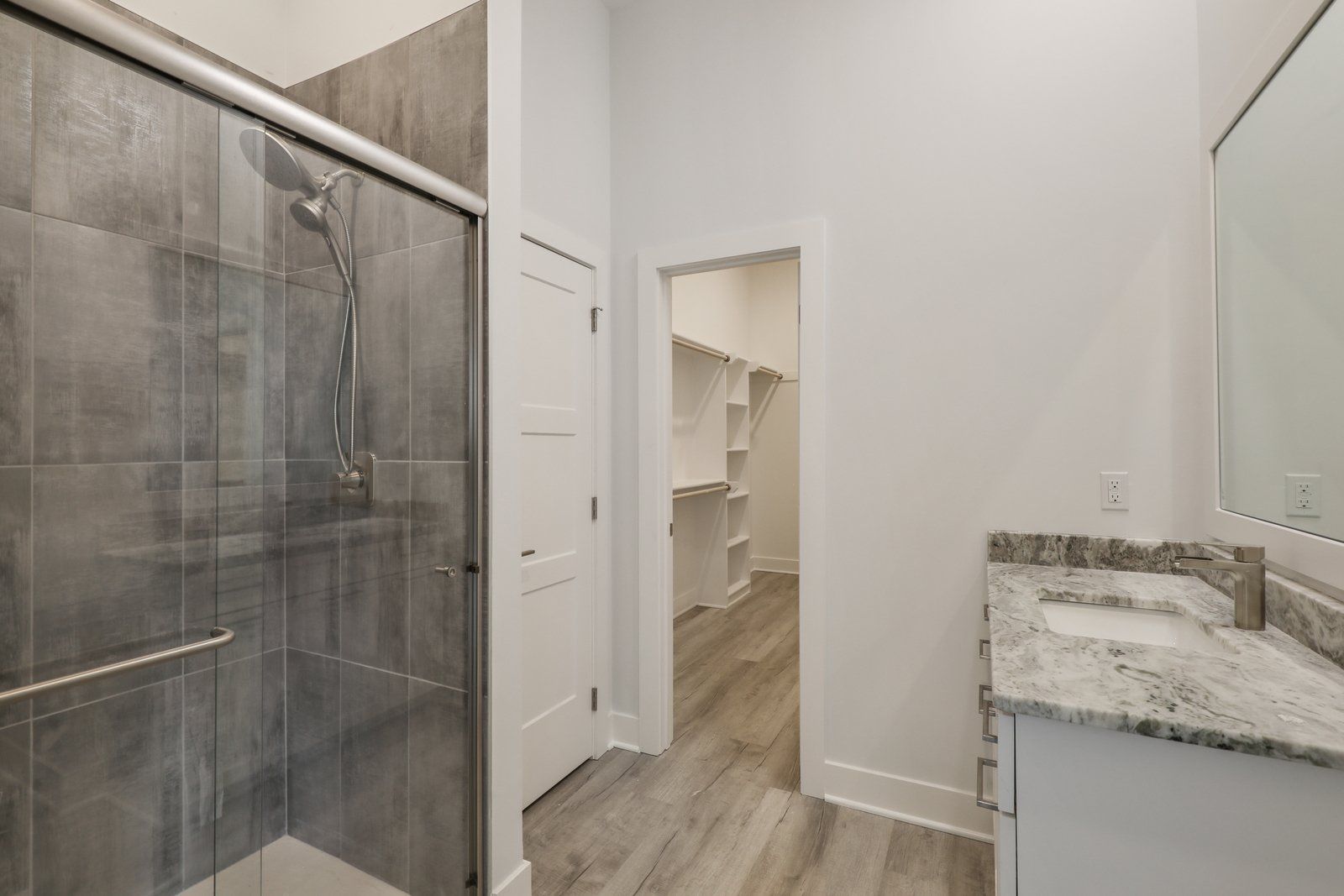 A bathroom with a walk in closet , shower , sink and mirror.