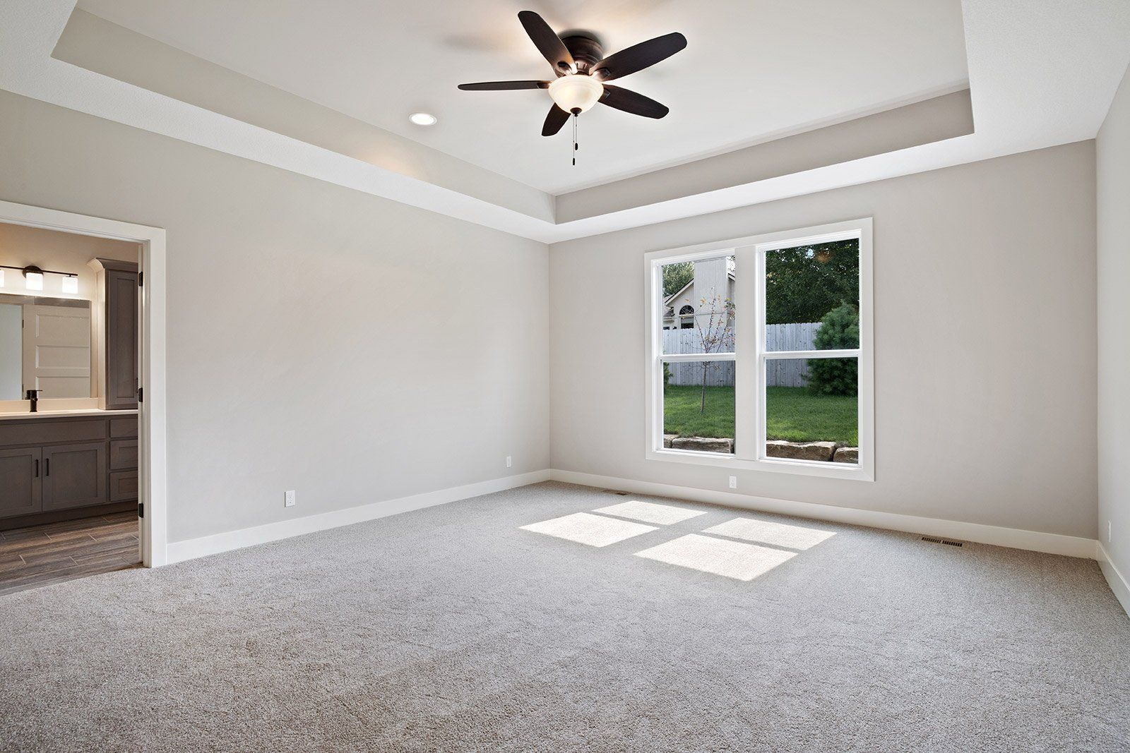 An empty bedroom with a ceiling fan and two windows.