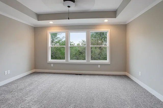 An empty bedroom with three windows and a ceiling fan.