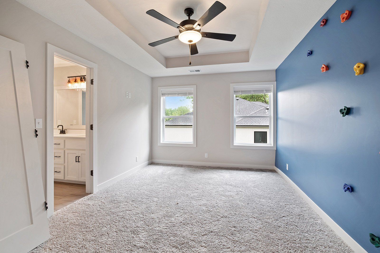 A bedroom with a climbing wall and a ceiling fan.