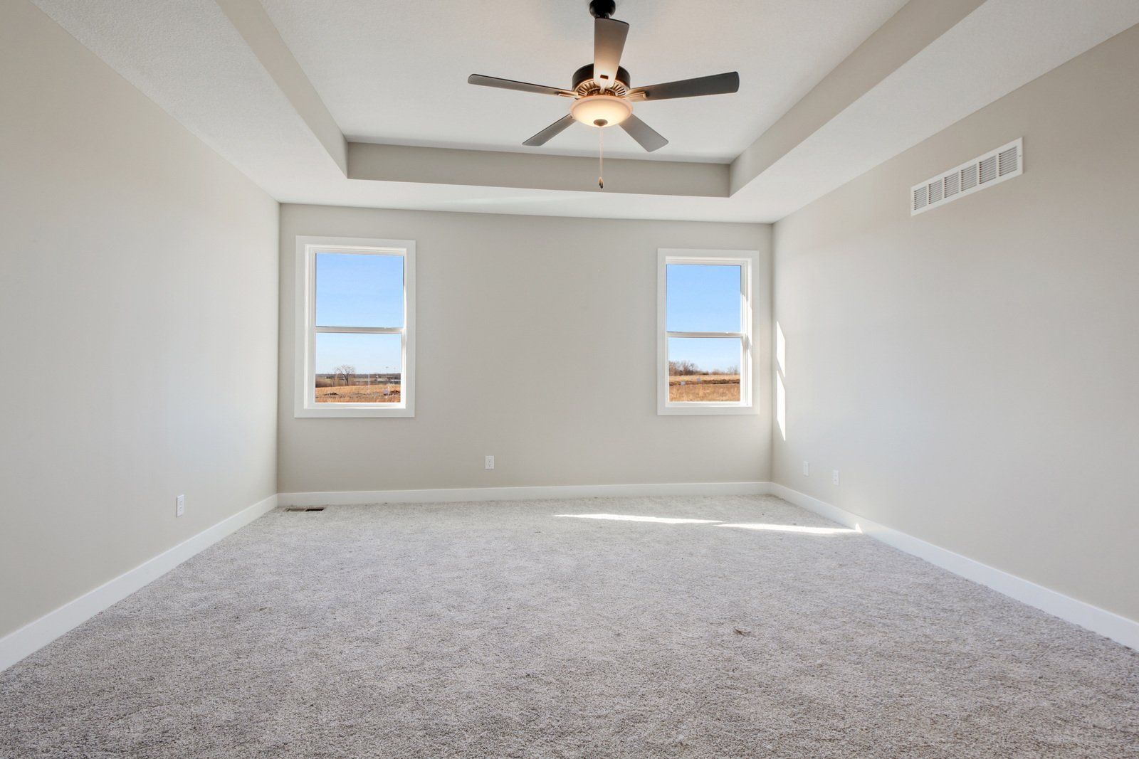 An empty bedroom with a ceiling fan and two windows