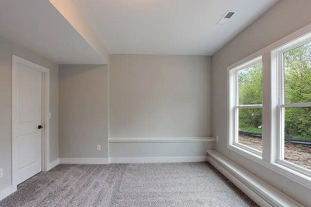 An empty room with a carpeted floor and three windows.