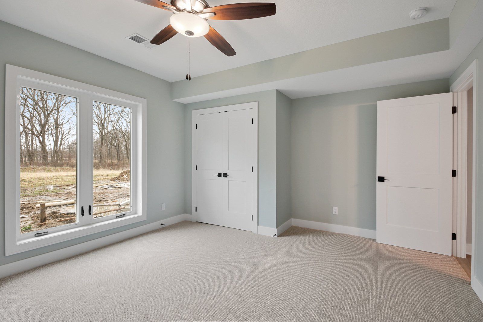 An empty bedroom with a ceiling fan and a large window.