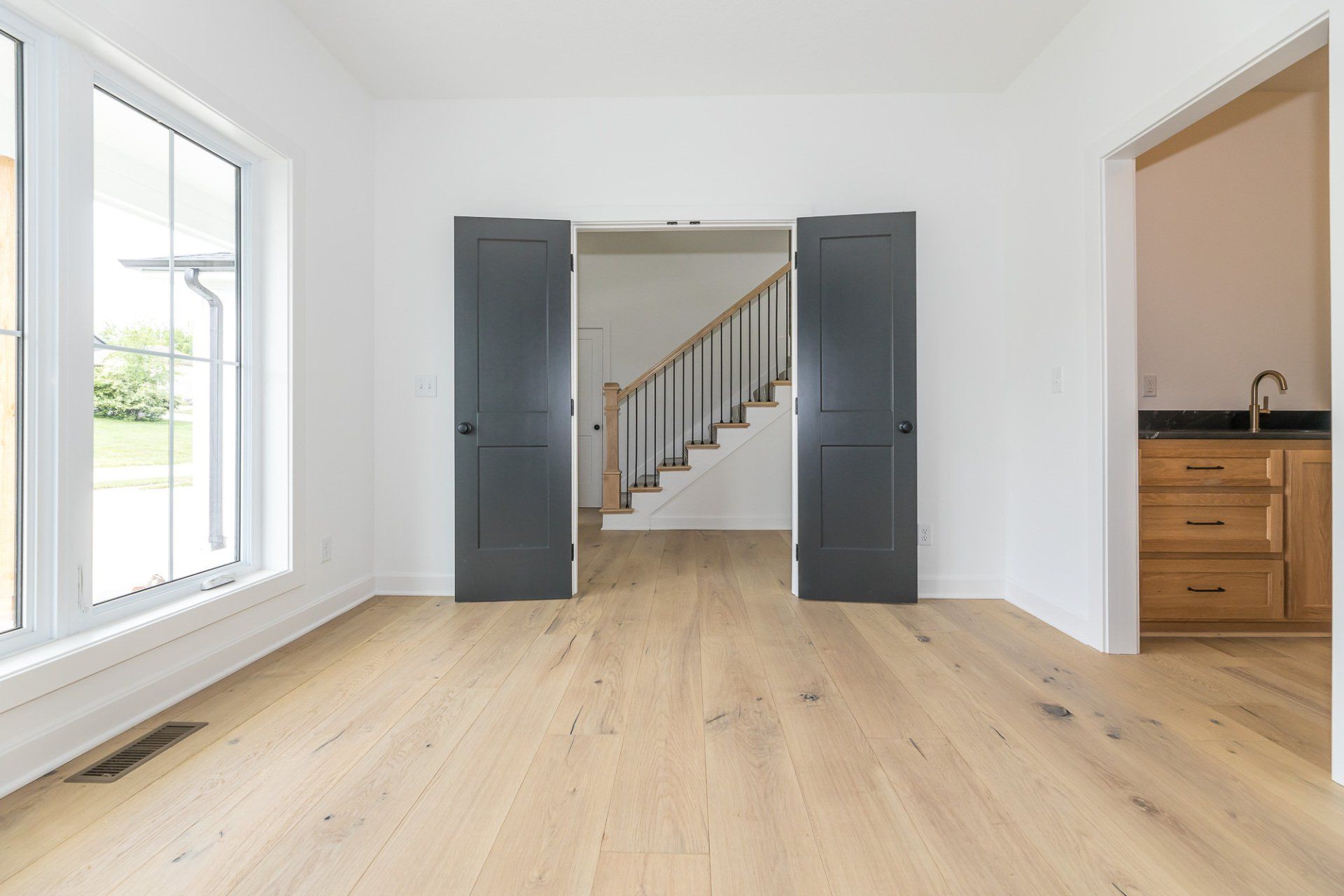 An empty living room with hardwood floors and black doors leading to a staircase.