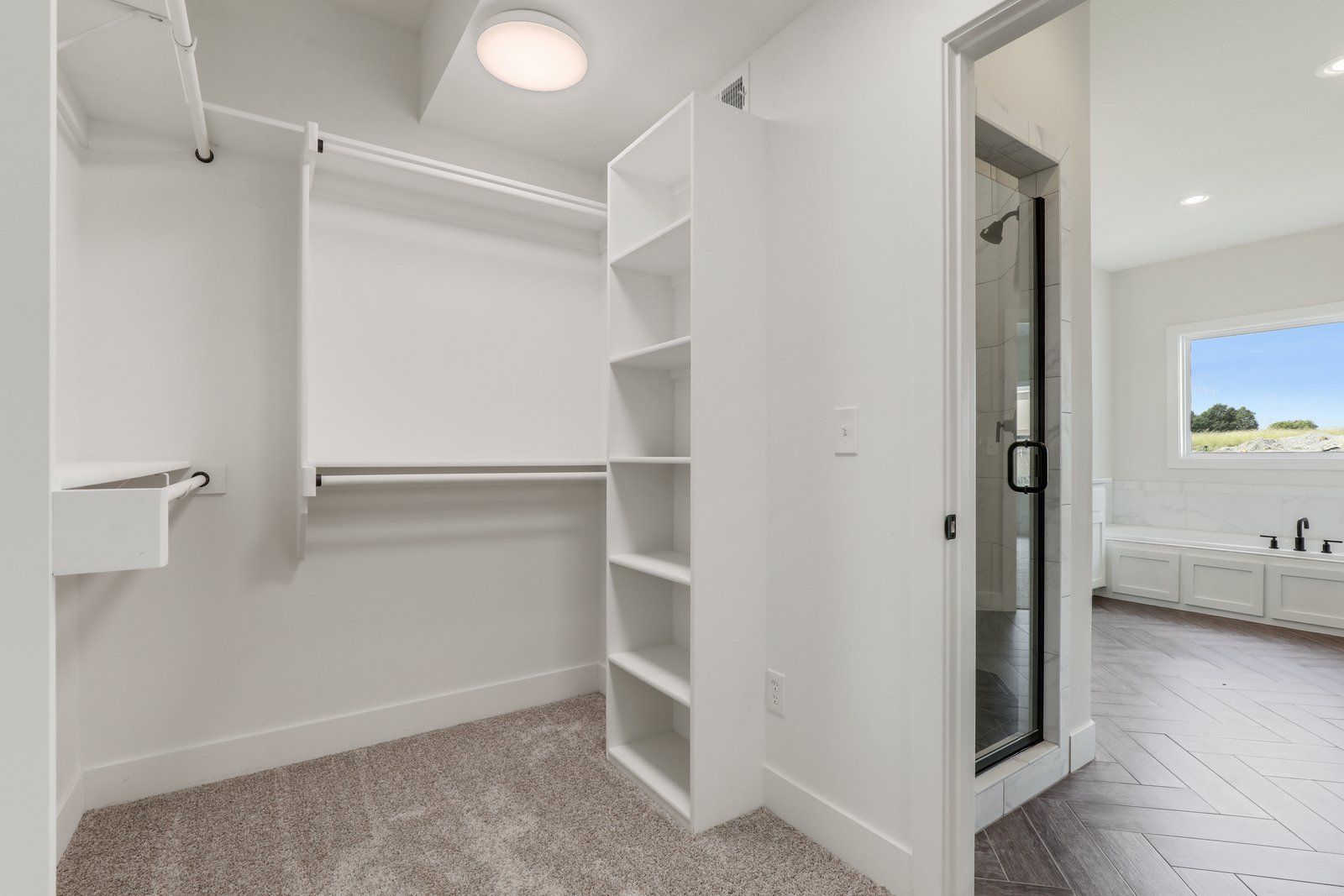 A walk in closet with lots of shelves and a bathroom in the background.