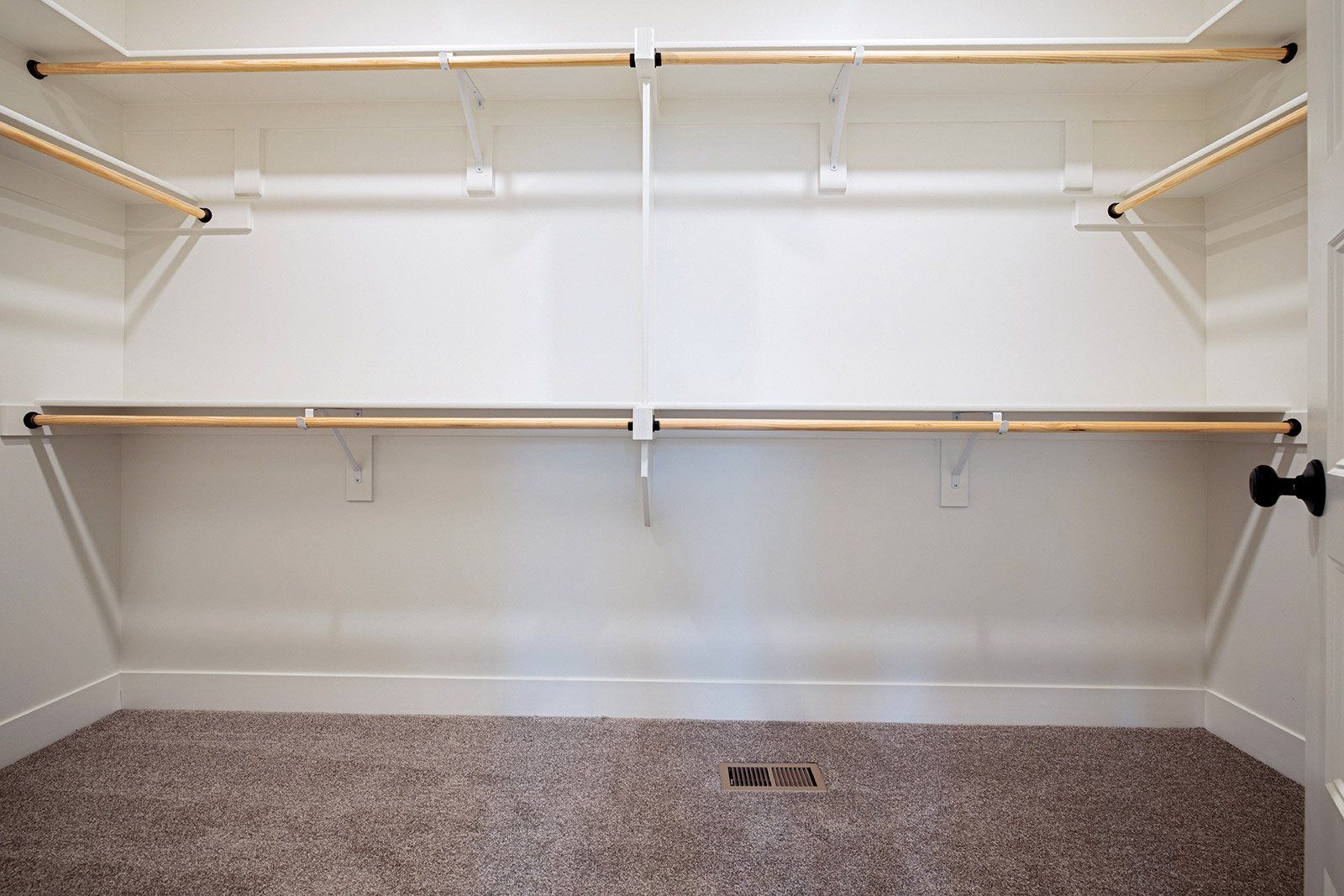An empty walk in closet with wooden shelves and a carpeted floor.