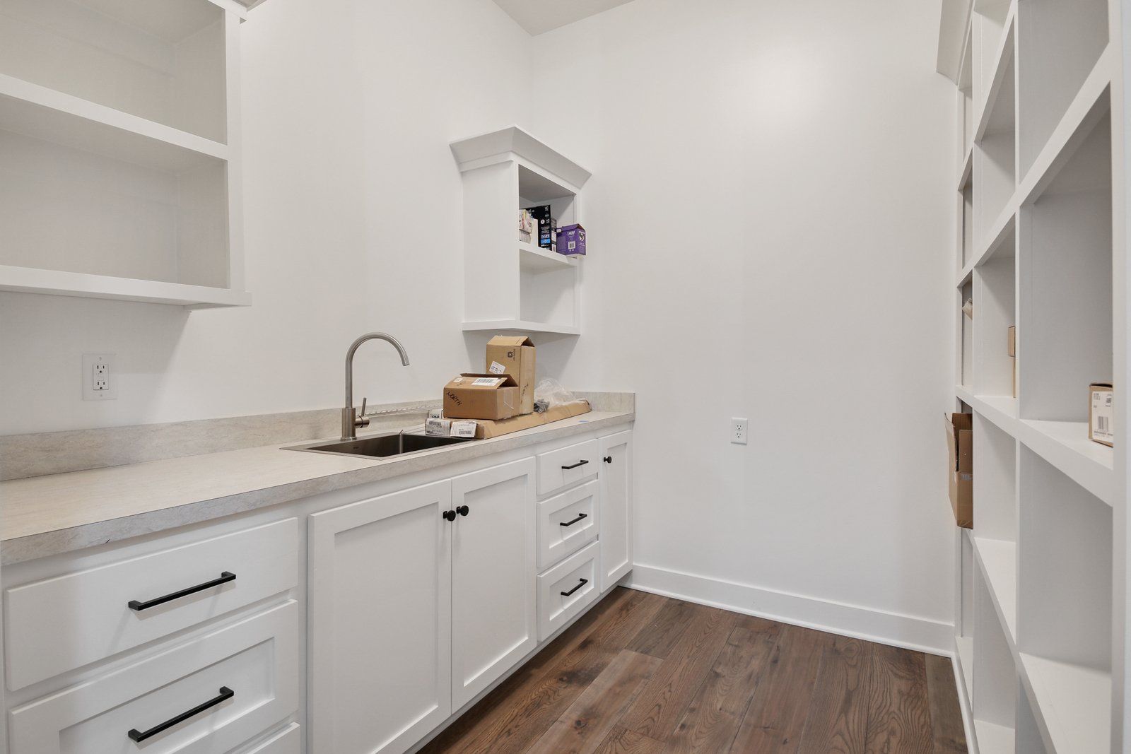 A kitchen with white cabinets , a sink , and shelves.