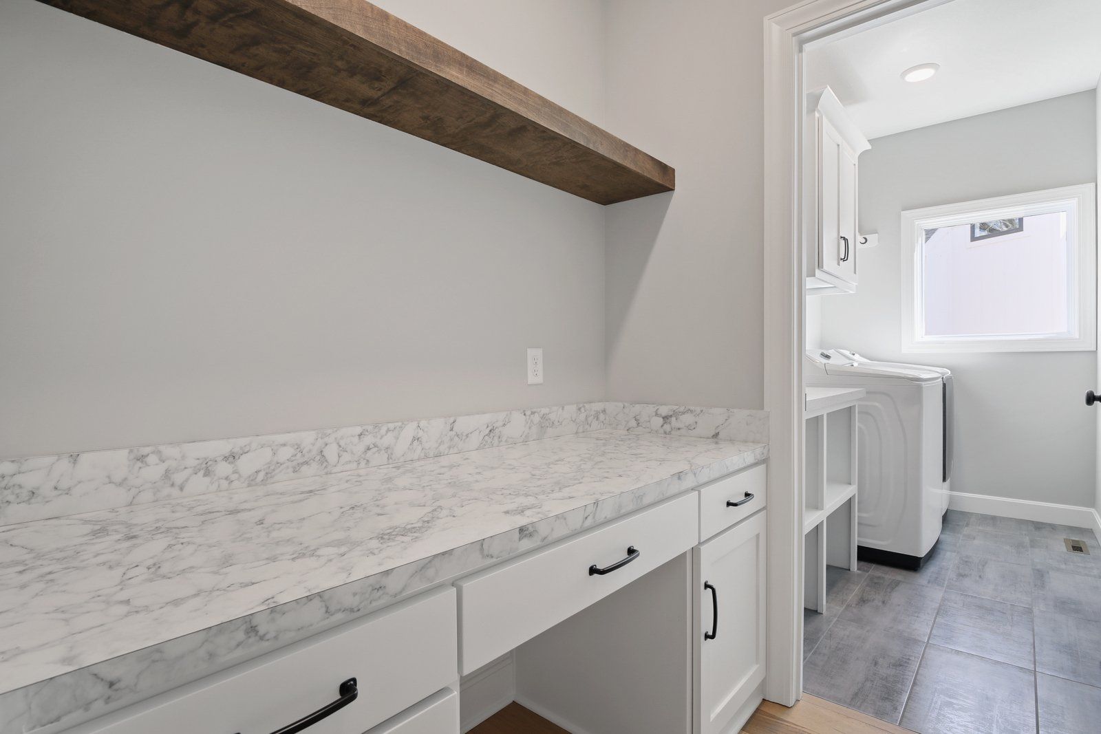A laundry room with a marble counter top and white cabinets.