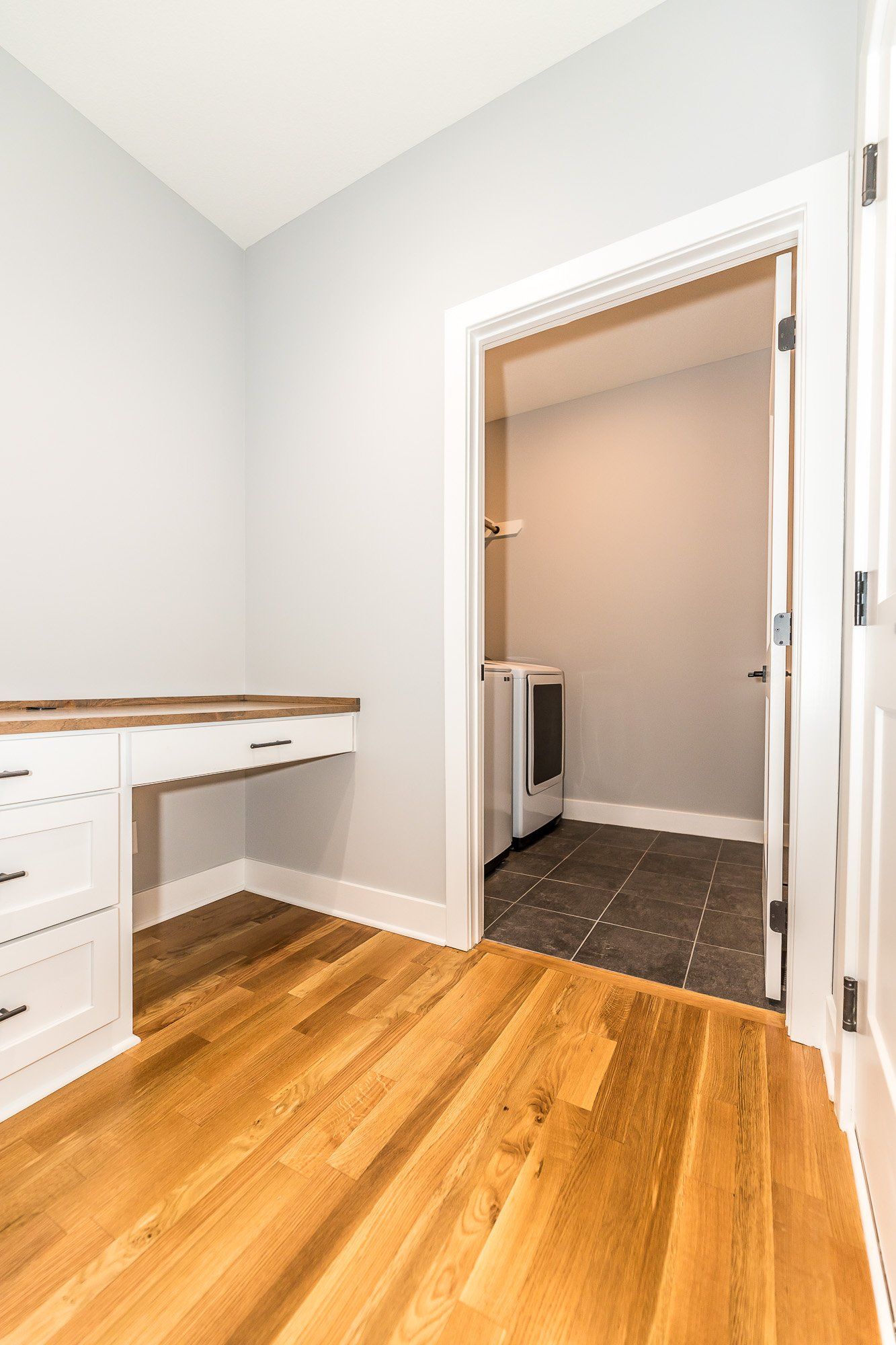 A room with a desk and drawers and a door that leads to a laundry room.