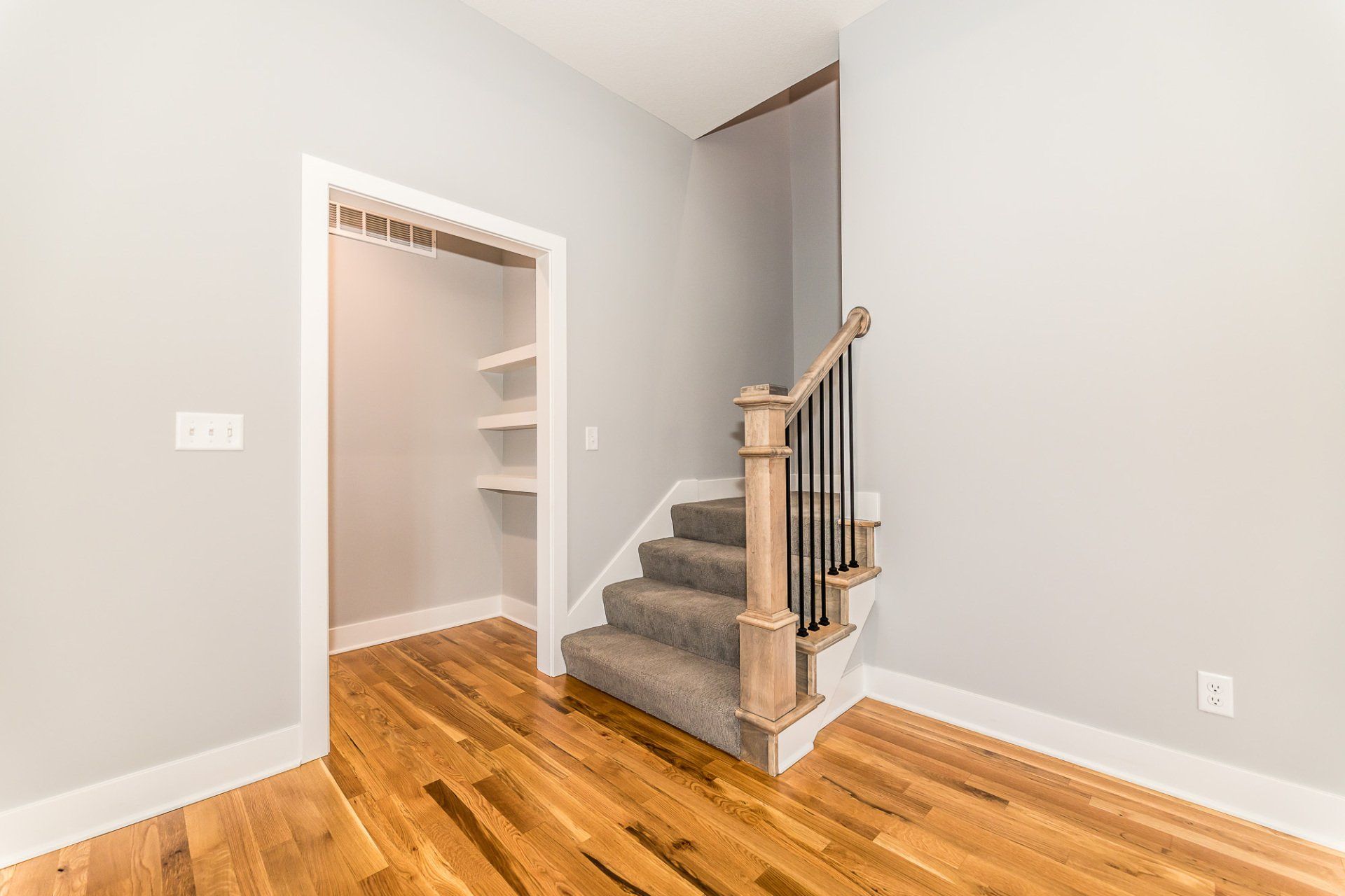 An empty room with hardwood floors and stairs leading to a walk in closet.