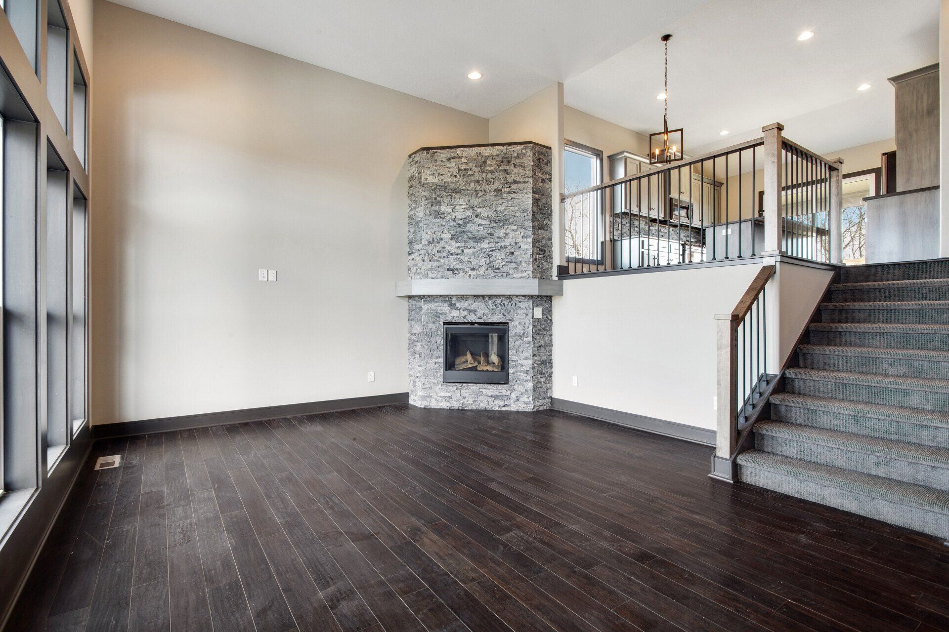 An empty living room with hardwood floors , stairs and a fireplace.