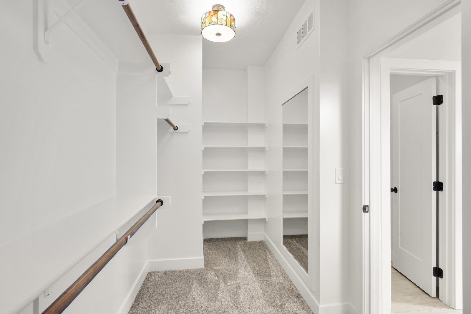 A walk in closet with lots of shelves and a mirror.