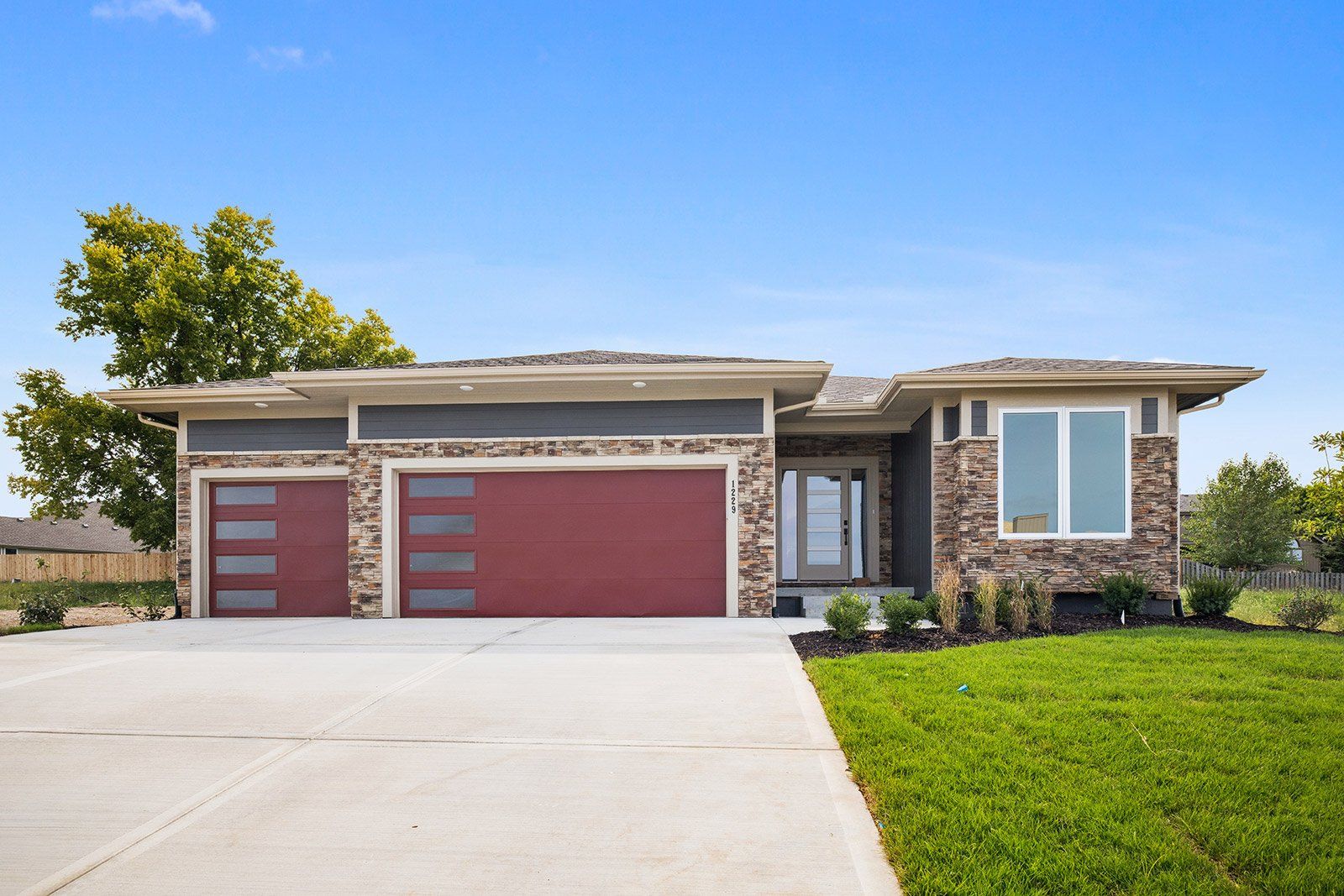 A modern house with a red garage door and a large driveway.