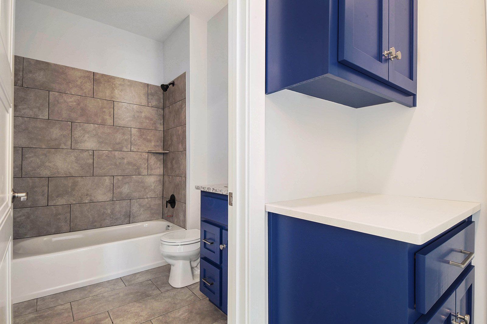 A bathroom with a bathtub , toilet , and blue cabinets.