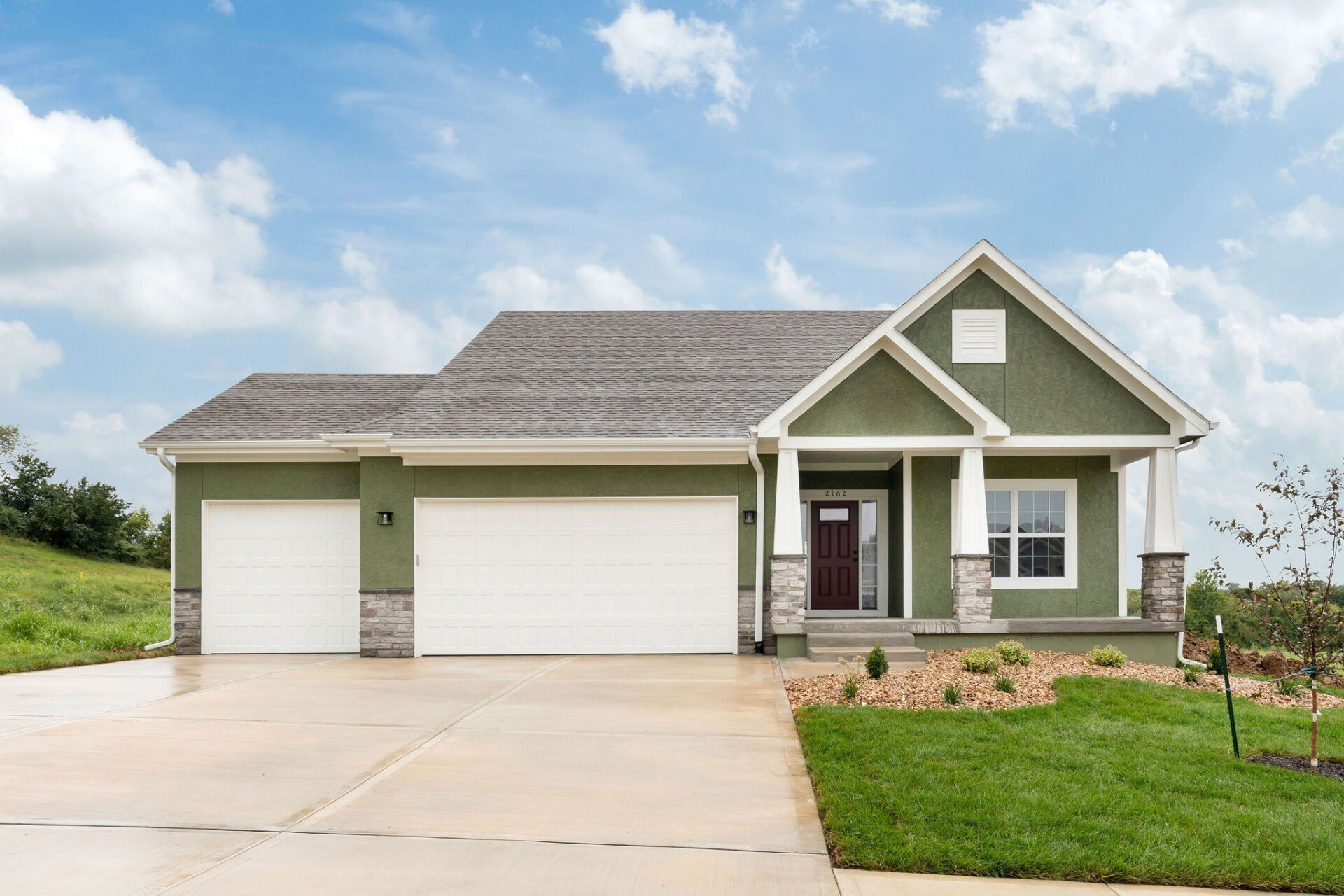 A green and white house with two garage doors and a driveway.