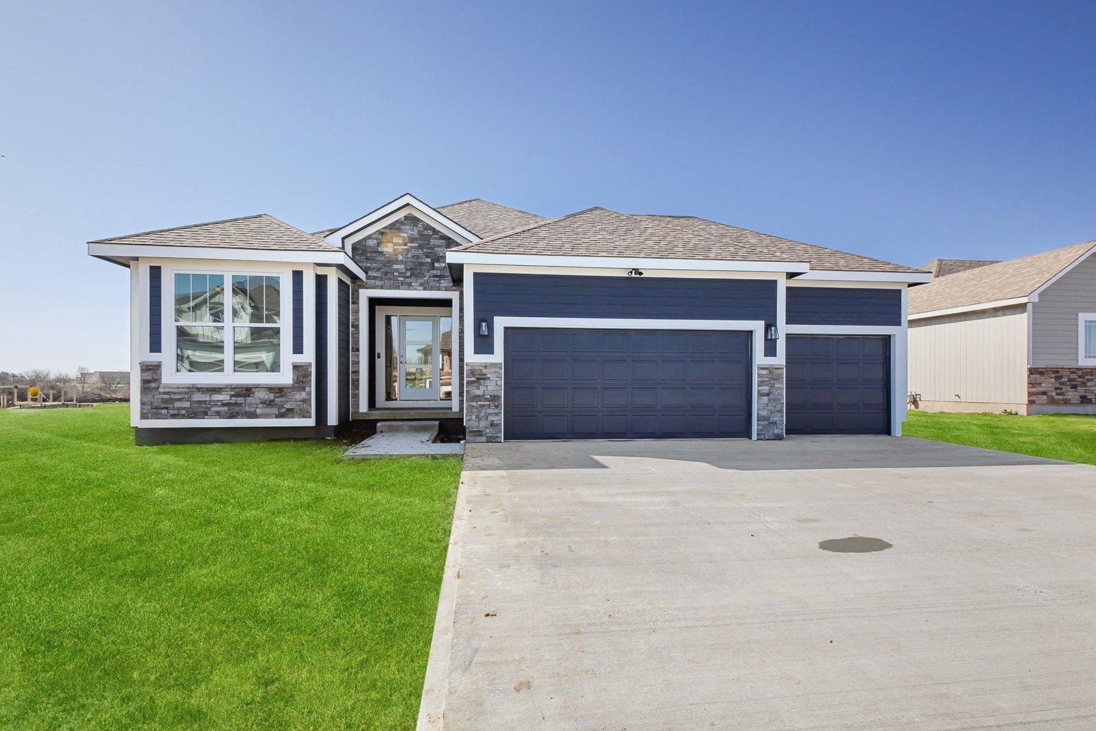 A house with a blue garage door is sitting on top of a lush green field.