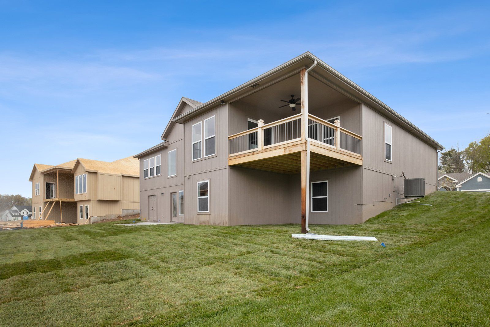 A large house with a large deck is sitting on top of a lush green hillside.