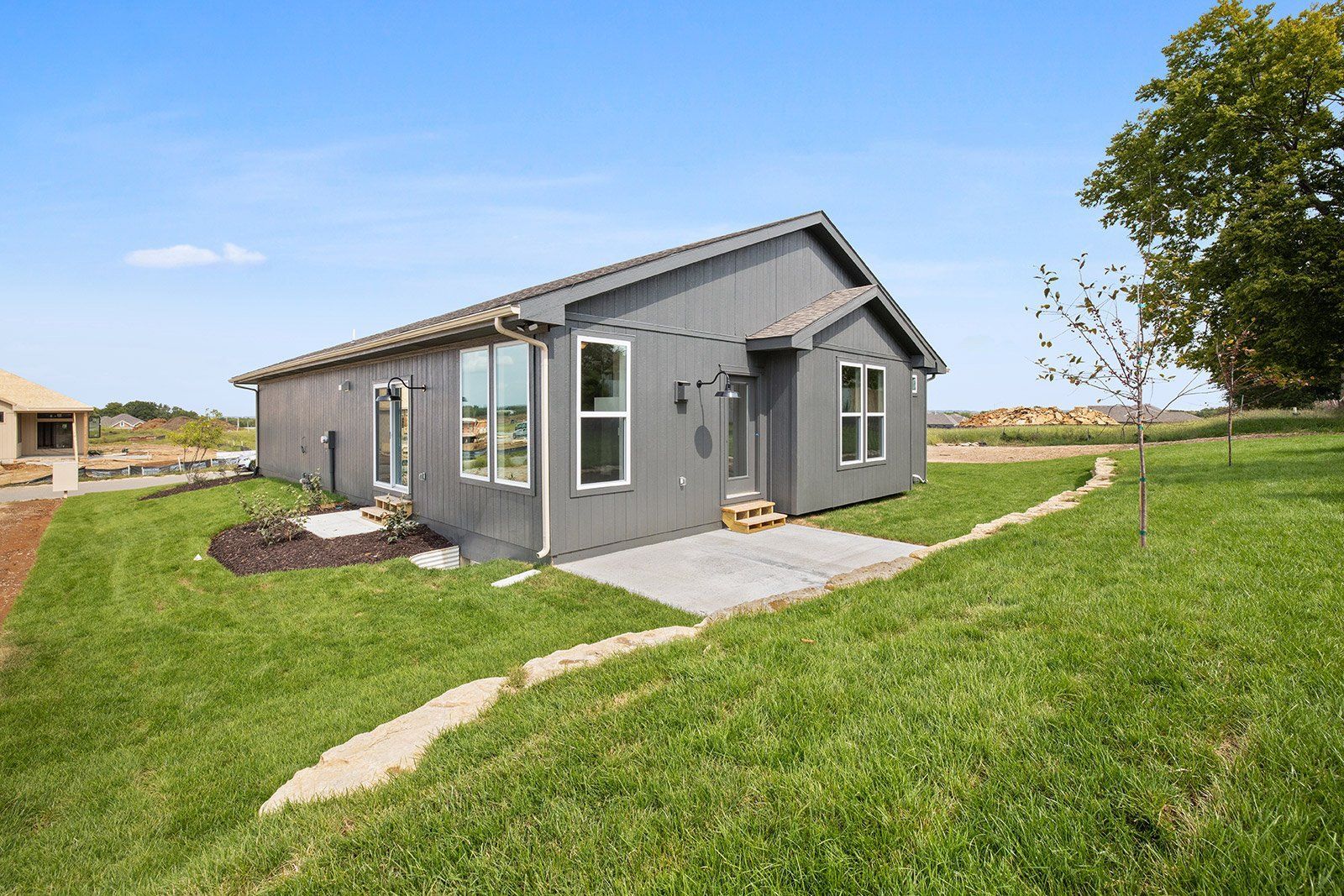 A small gray house is sitting in the middle of a lush green field.
