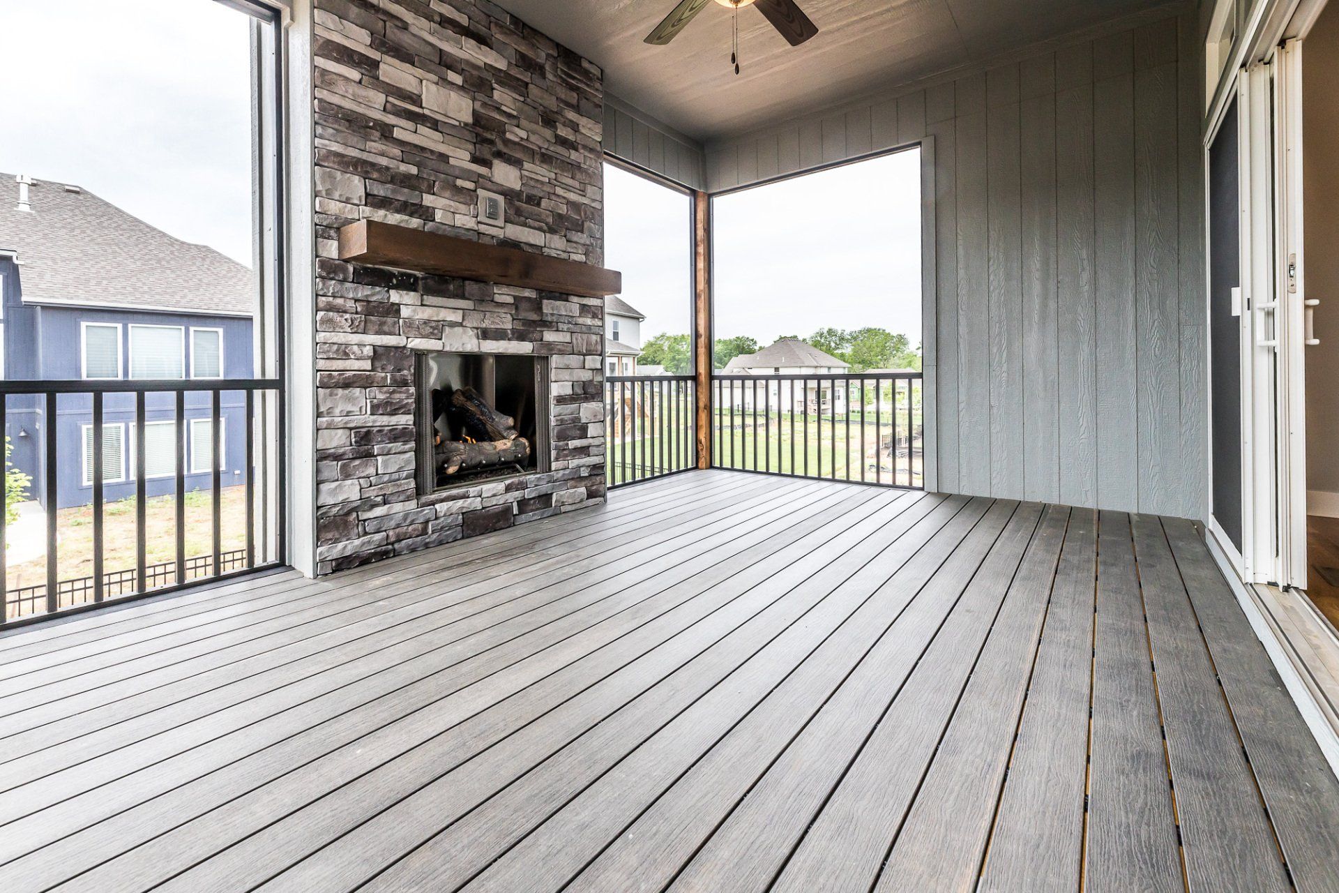 A screened in porch with a fireplace and a ceiling fan.