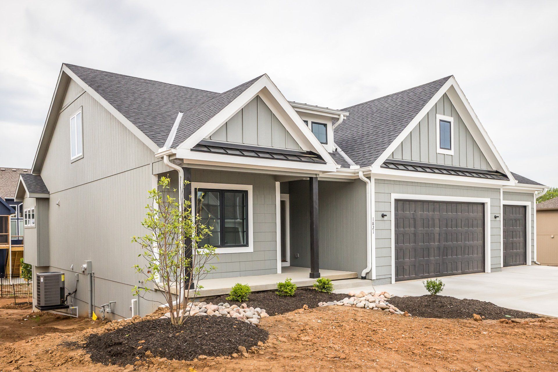 A gray house with a gray roof and two garage doors is sitting on top of a dirt field.