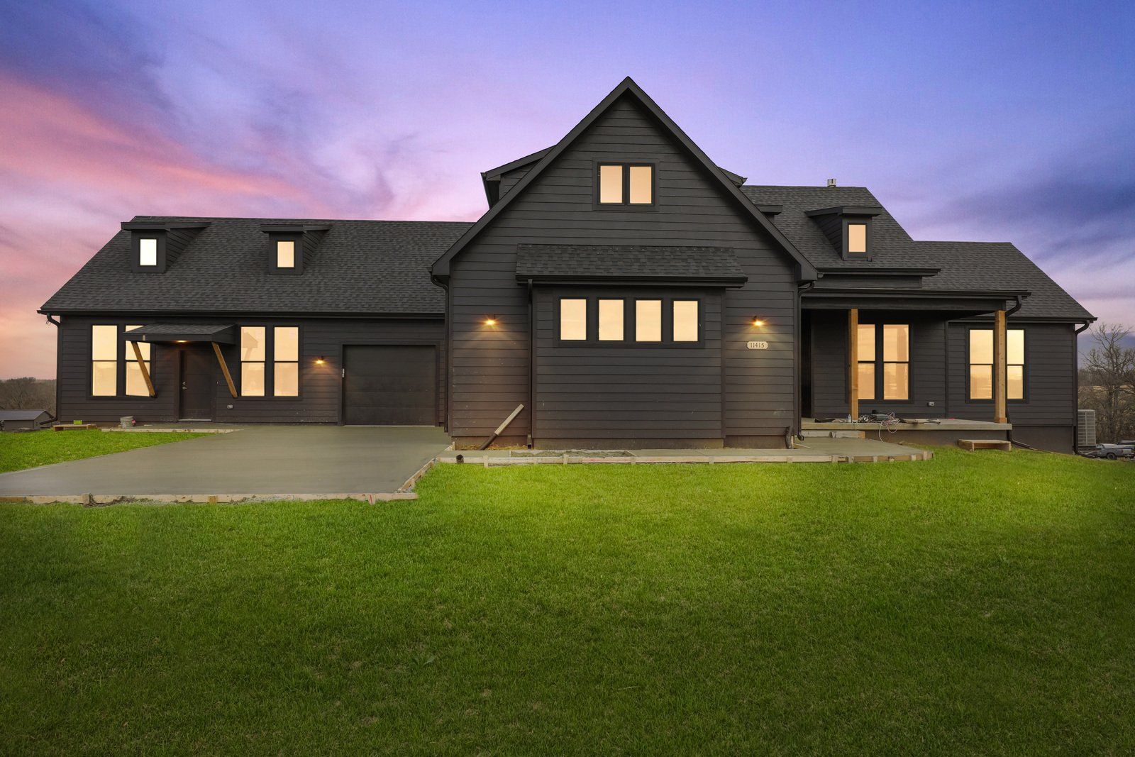 A large black house with a lot of windows is sitting on top of a lush green field.