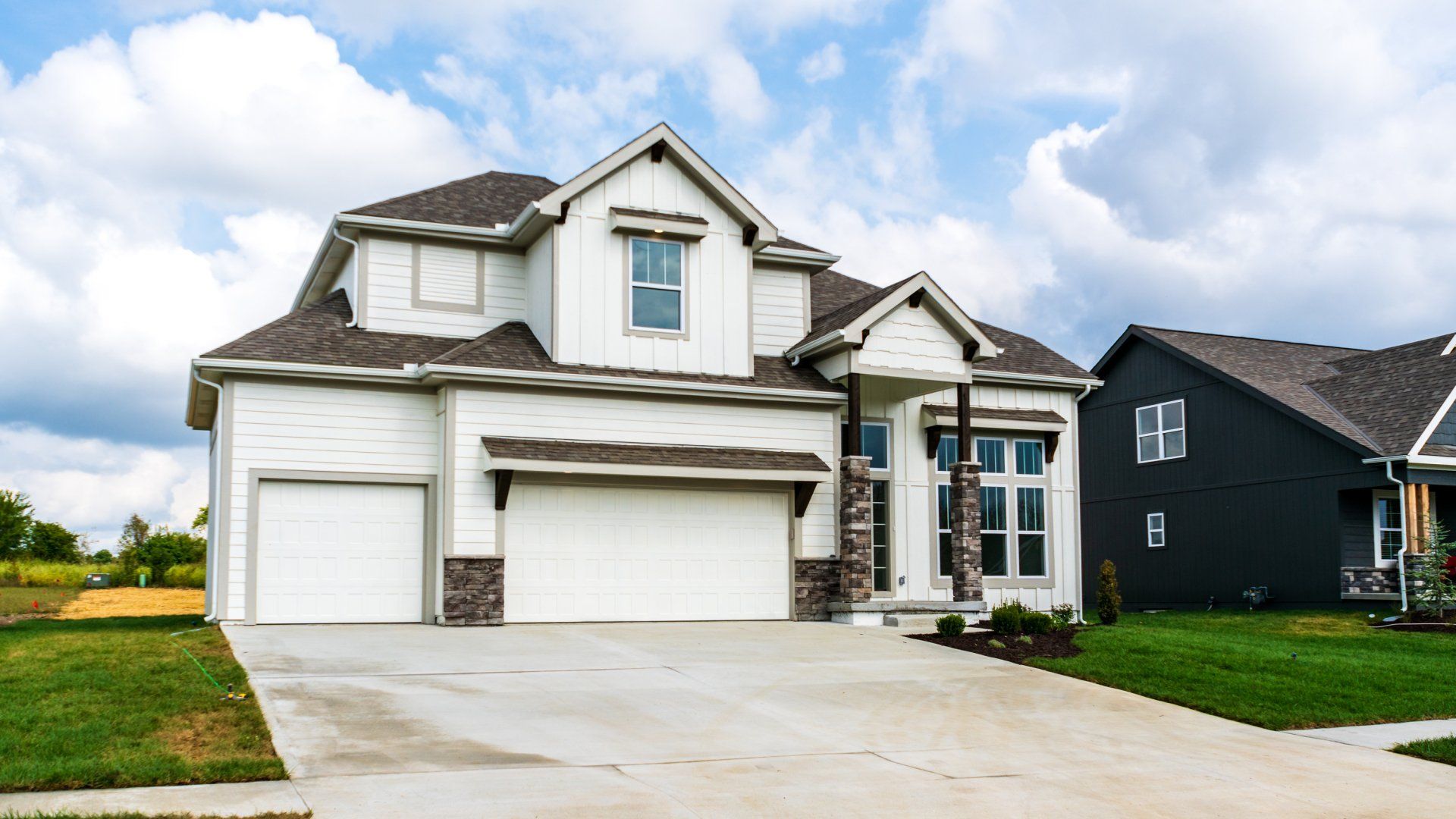 A large white house with a large driveway and a black house in the background.