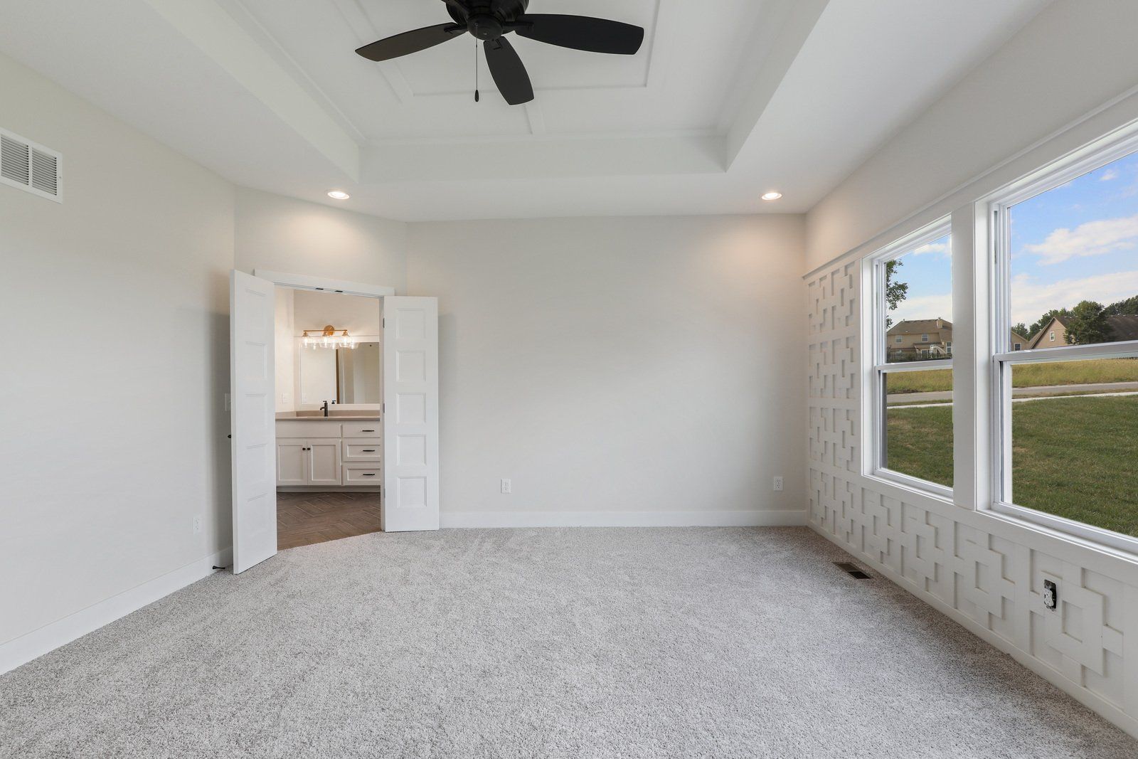 An empty bedroom with a ceiling fan and two windows.