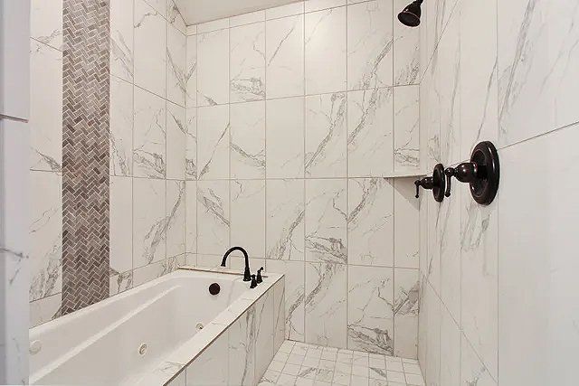 A bathroom with marble tiles , a tub and a shower.