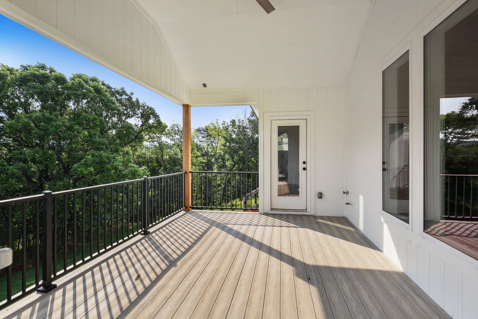 A large empty deck with a ceiling fan and trees in the background