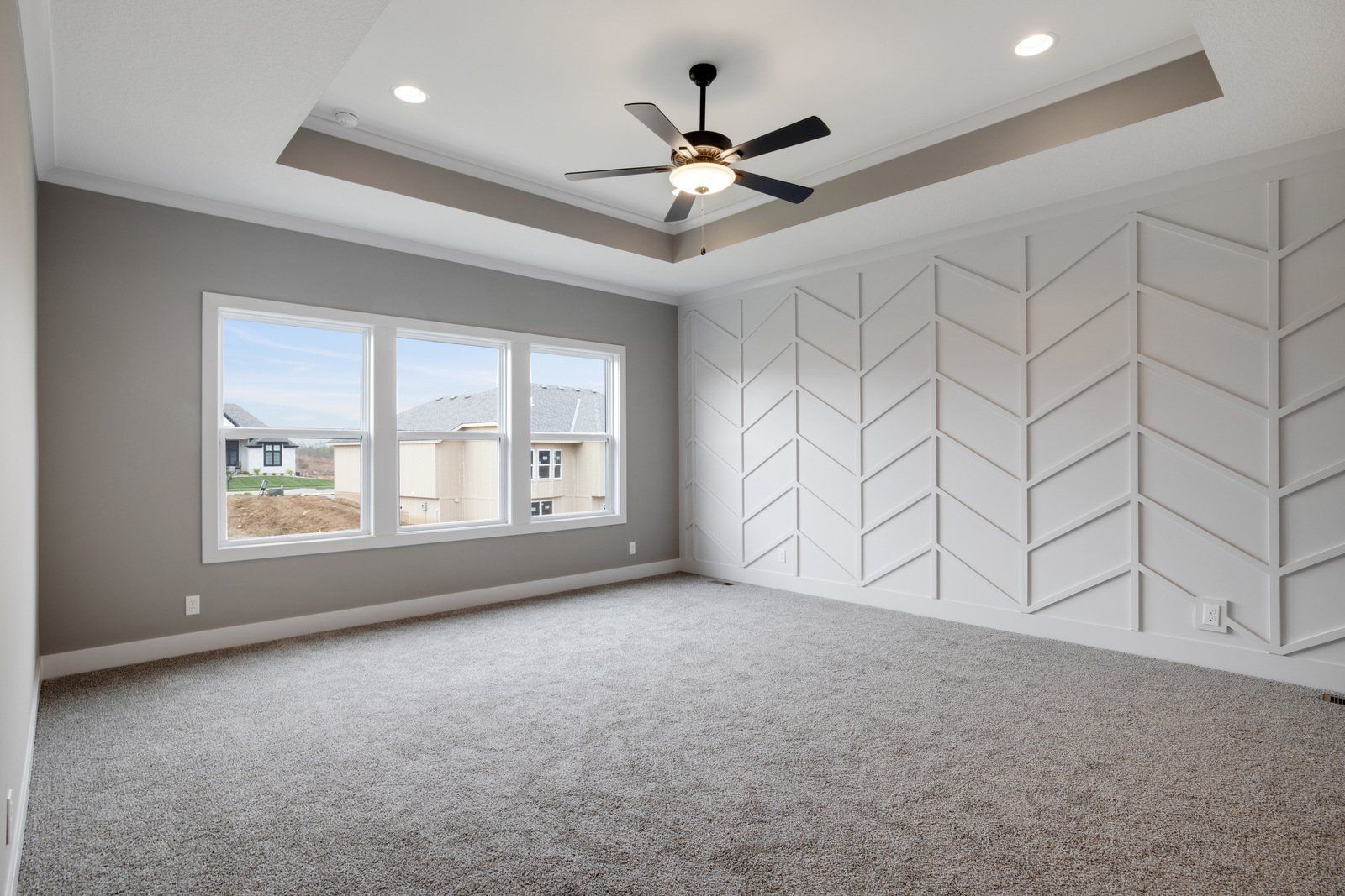 An empty bedroom with a ceiling fan and a chevron wall.