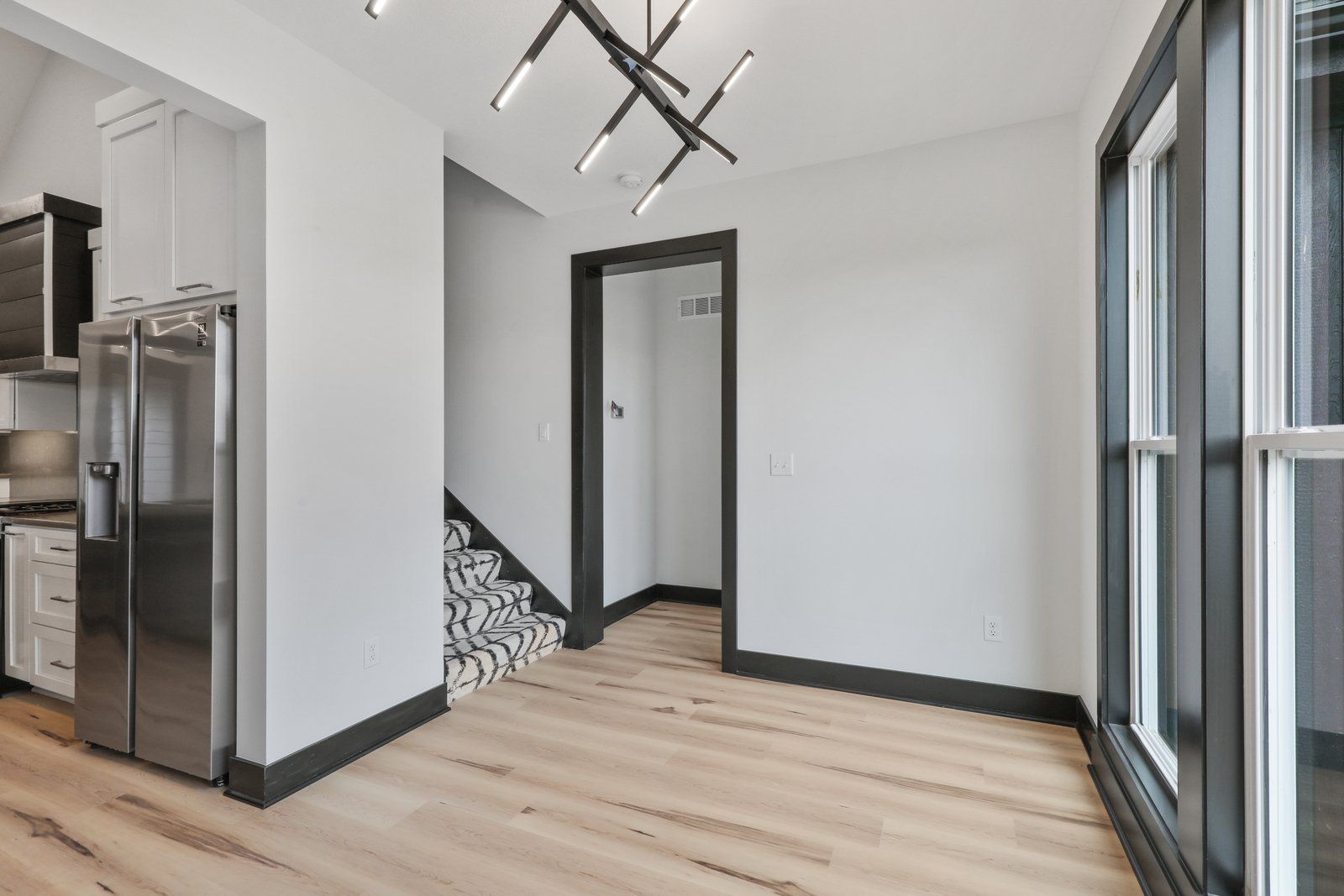 An empty room with a refrigerator , stairs , and windows.