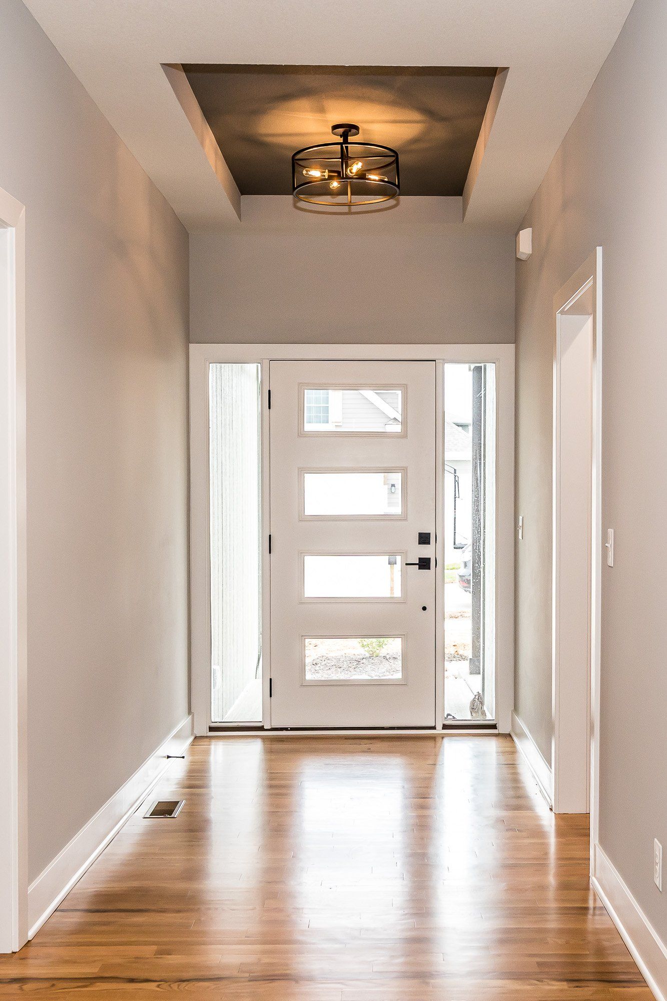 A hallway with a white door and a chandelier hanging from the ceiling.