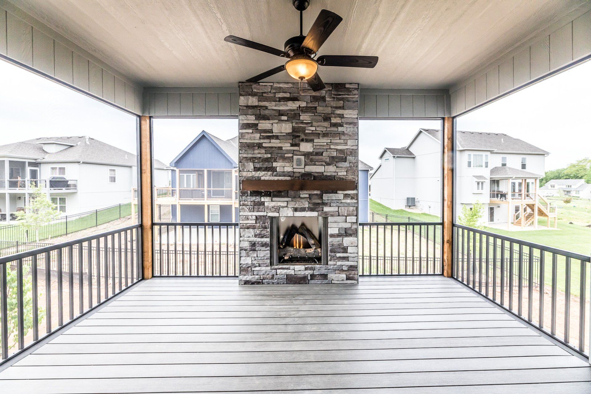 A screened in porch with a fireplace and ceiling fan.