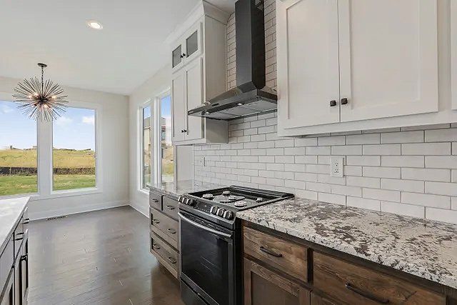 A kitchen with white cabinets , granite counter tops , a stove and a window.