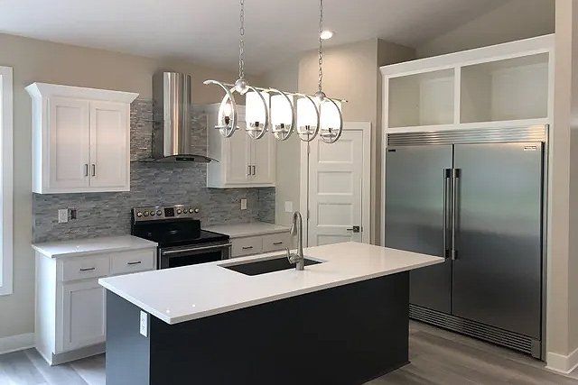 A kitchen with stainless steel appliances , white cabinets , a sink , and a large island.
