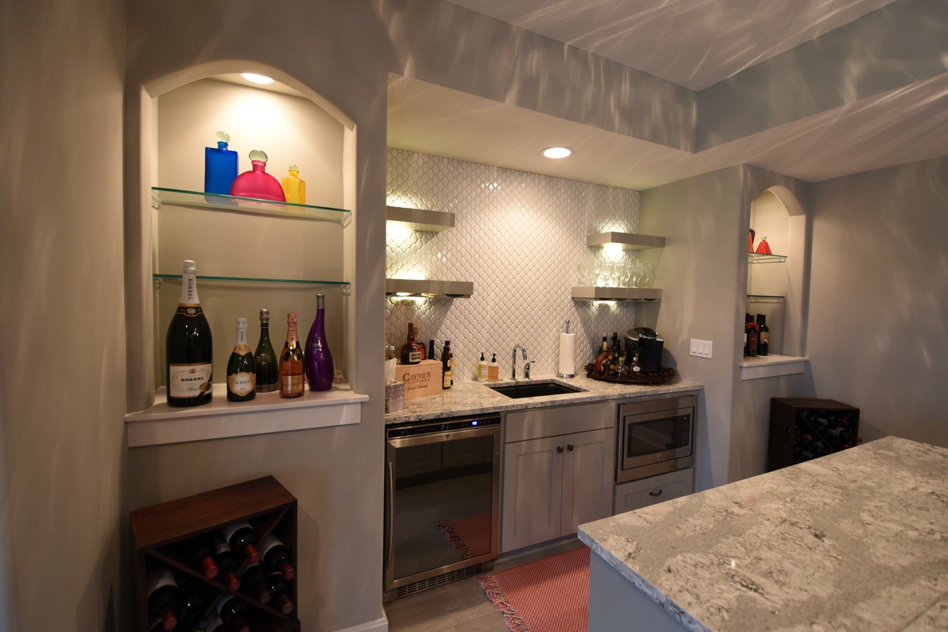 A kitchen with a bar and bottles of wine on shelves.