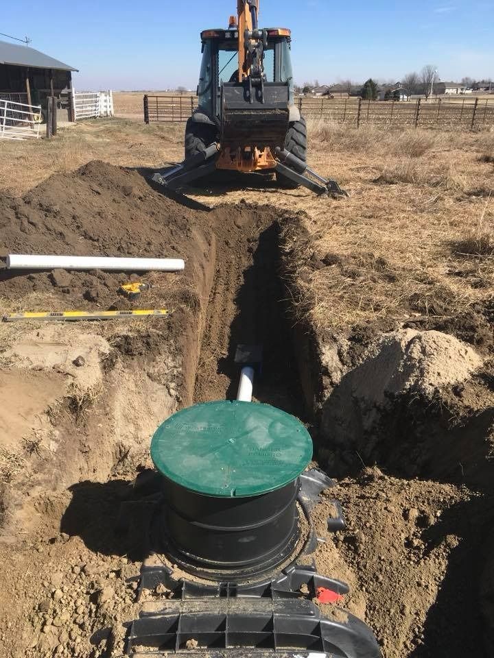 Backhoe at work installing a septic tank in a field with green lid in view.