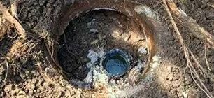 A hole in the ground with a pipe visible inside, surrounded by dirt and roots.