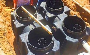 Black septic tank system being installed in a sandy trench; a level is used to assess alignment.