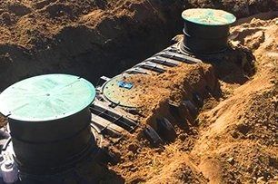 An open trench reveals an installed septic system with three circular, green-lidded access points.