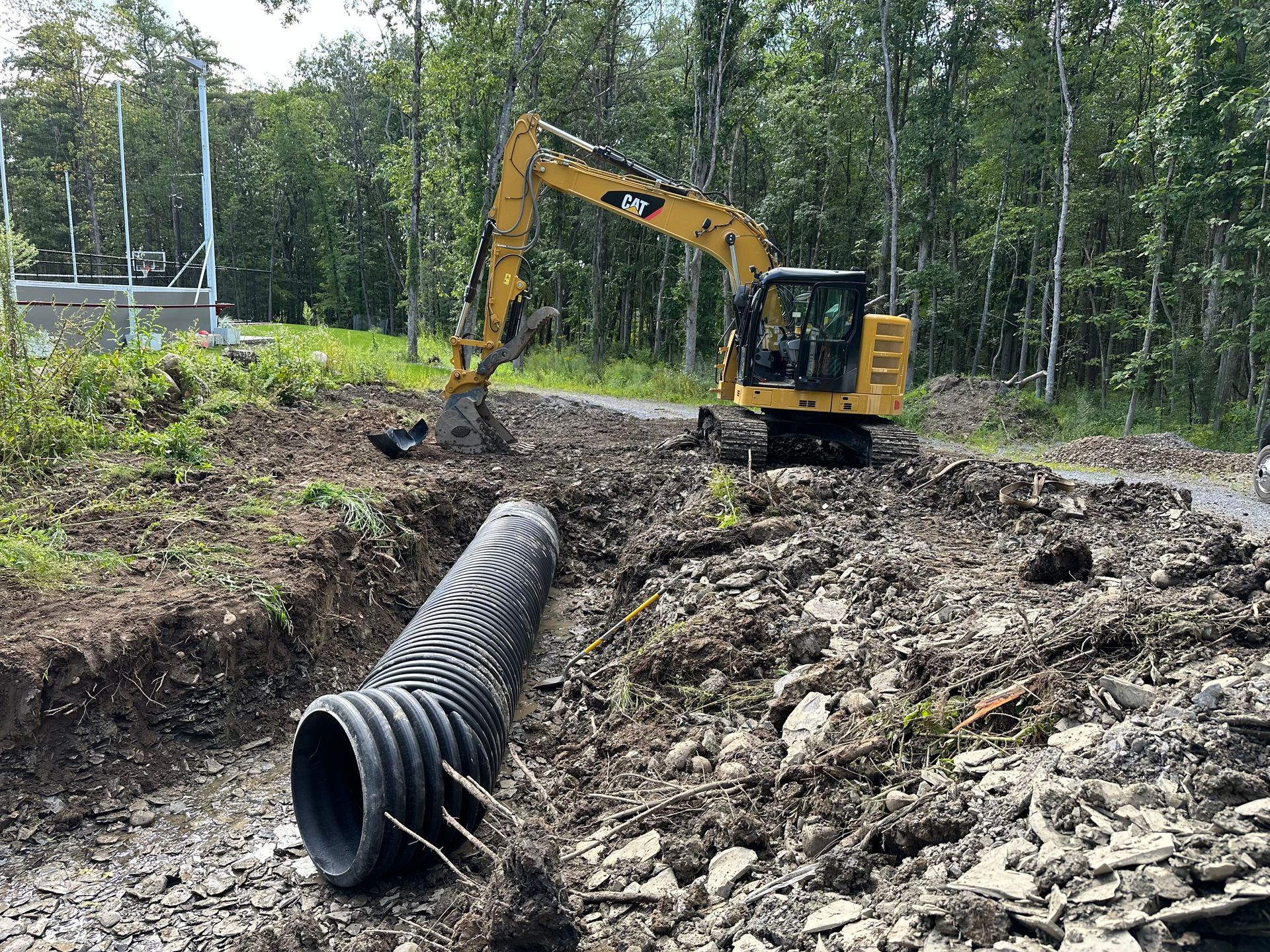 A yellow excavator is digging a hole in the dirt next to a large pipe