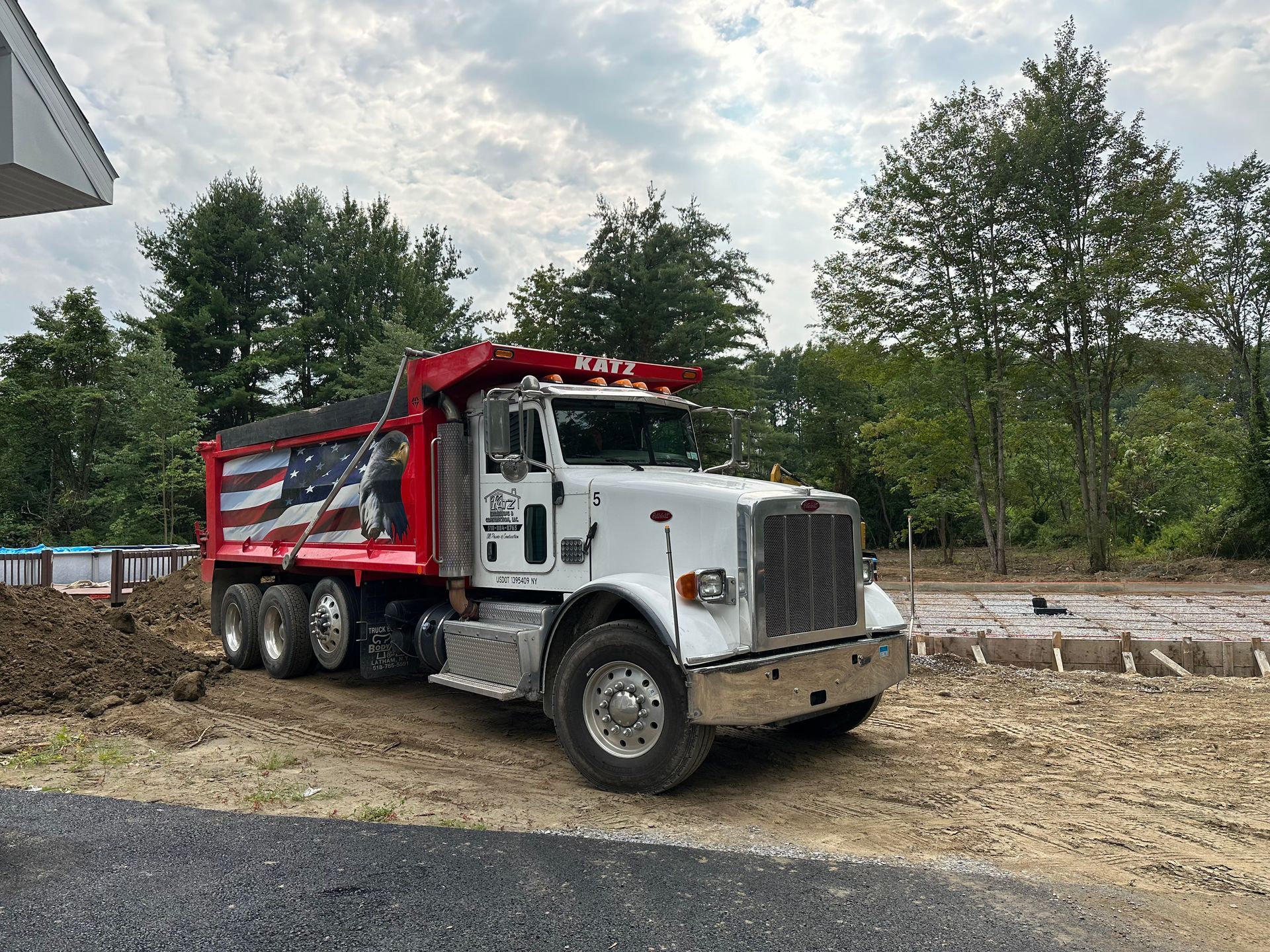 A white dump truck with an american flag on the side is parked in a dirt lot