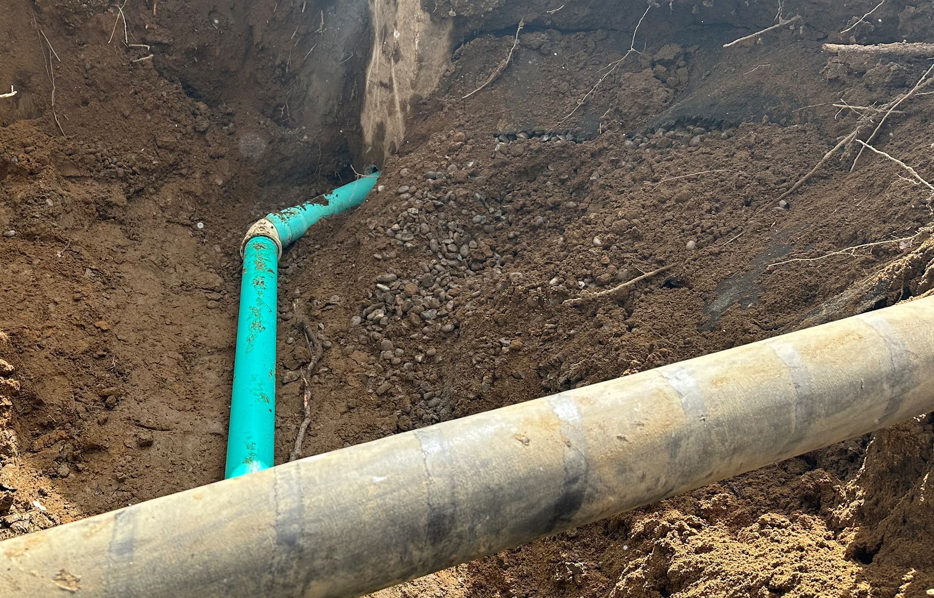 A blue pipe is laying in the dirt next to a large pipe