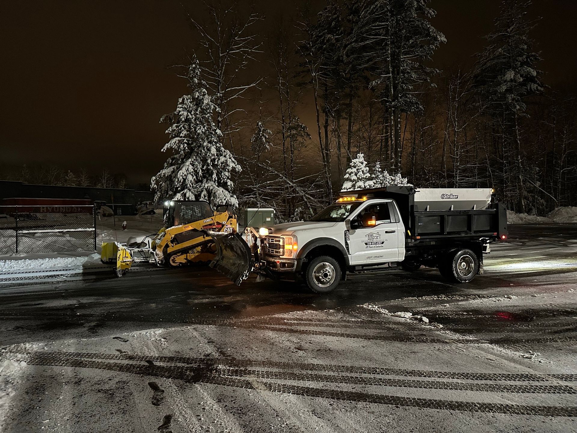 A snow plow is plowing snow in a parking lot at night