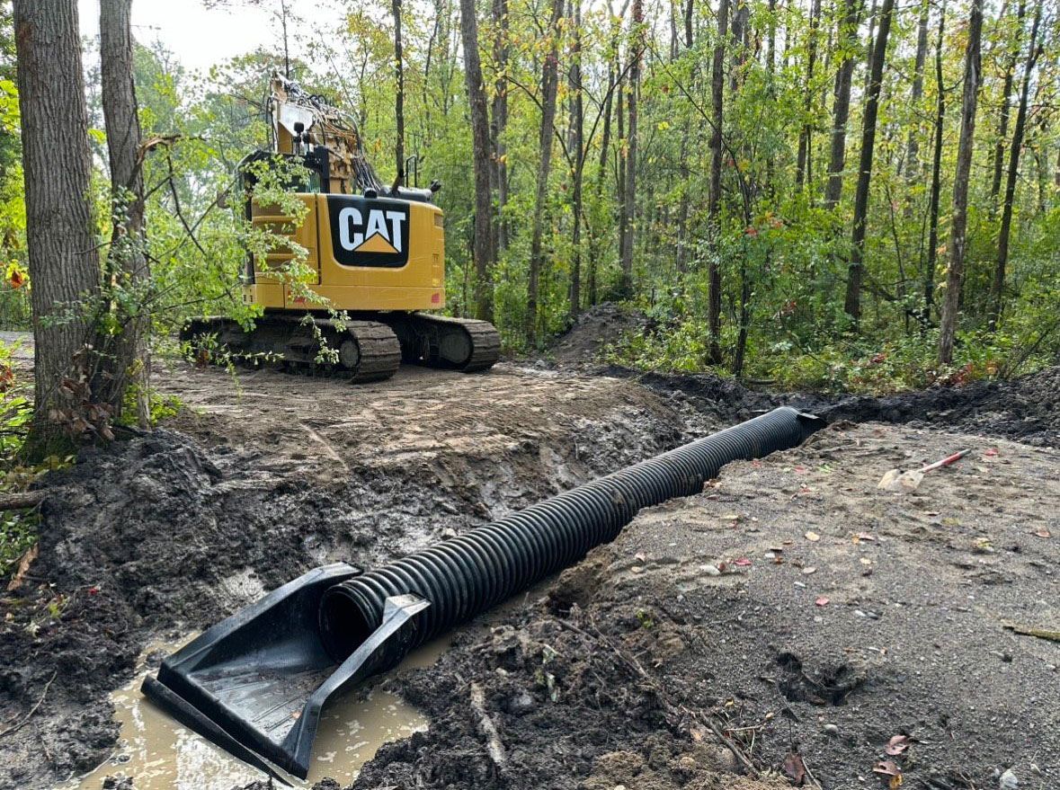A cat excavator is working on a muddy road in the woods