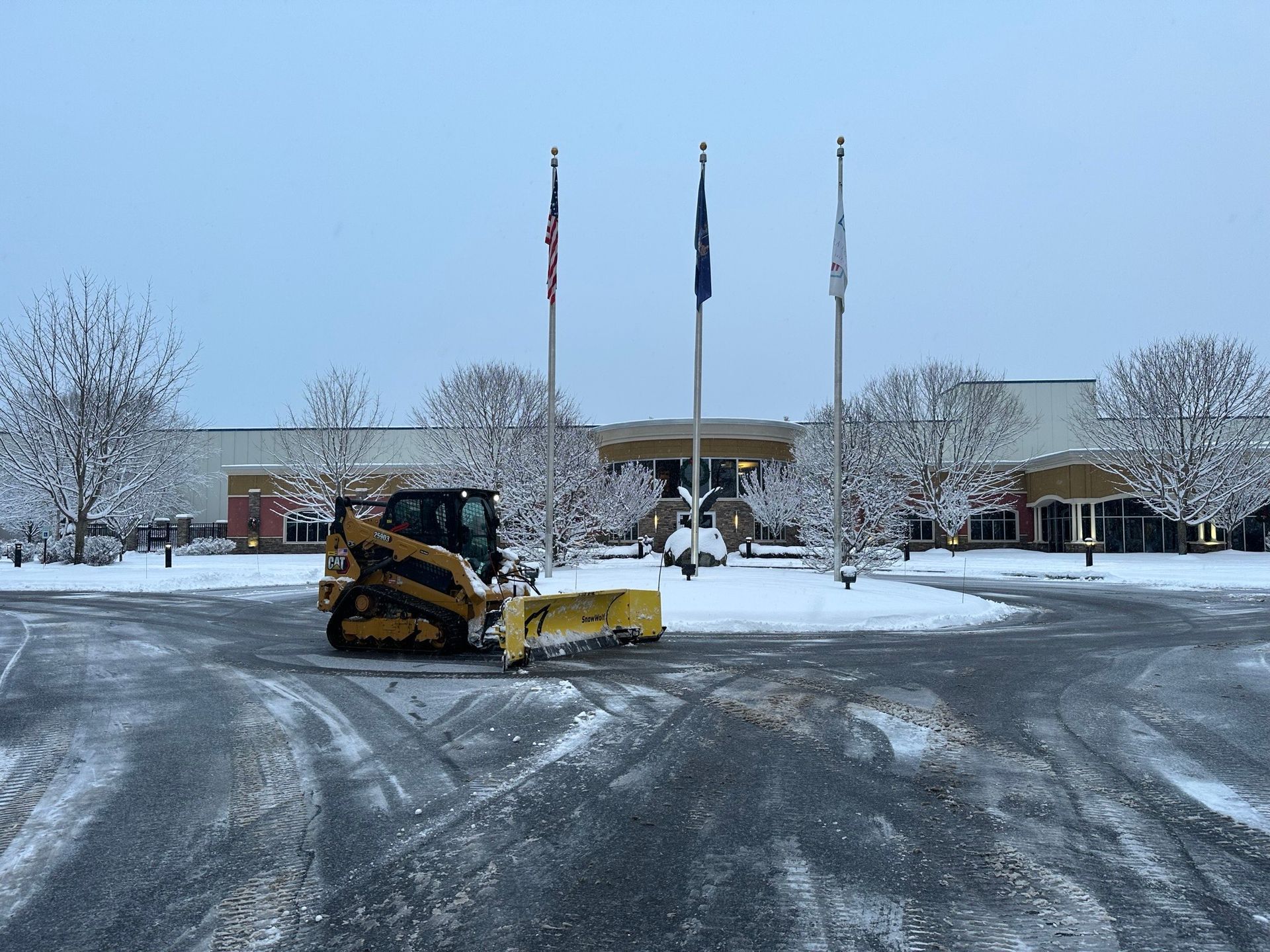 A snow plow is plowing a parking lot in front of a building