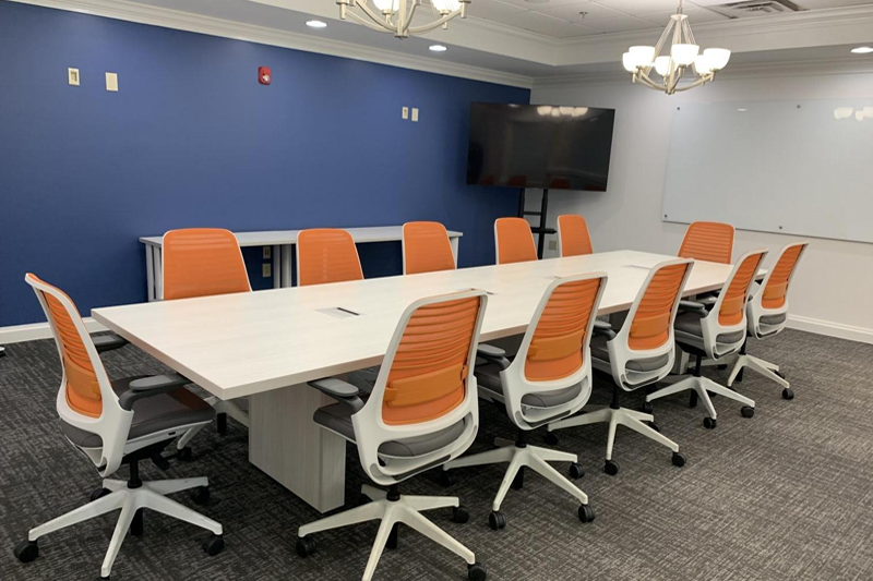 A conference room with a long table and orange chairs.