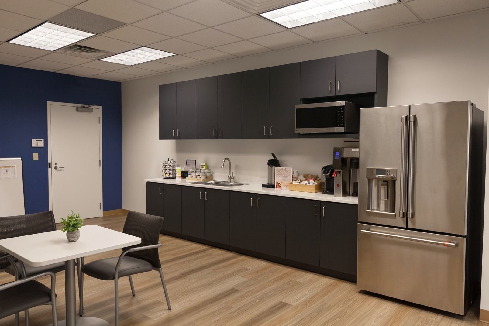 A kitchen with stainless steel appliances , black cabinets , a table and chairs.